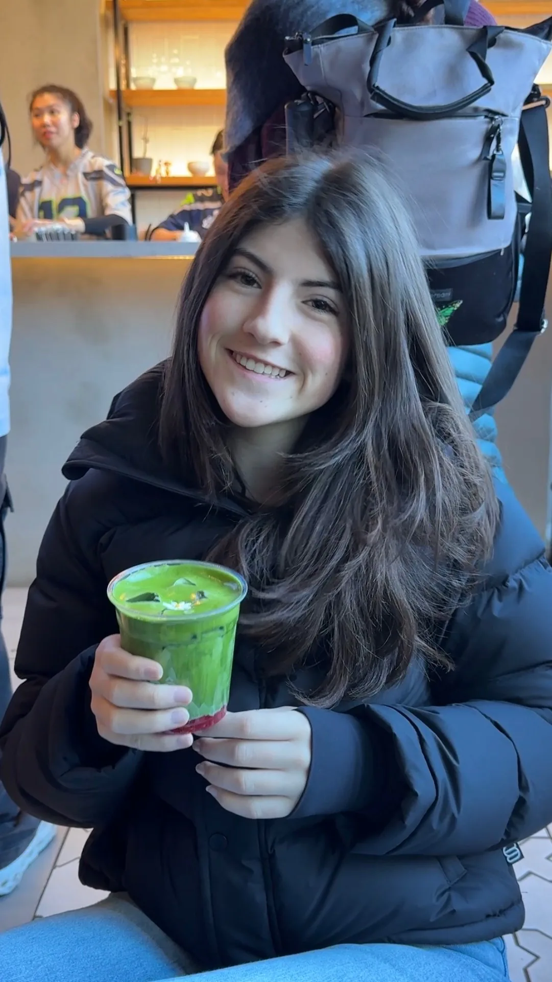 Skylar Cantando smiling in a cafe, holding an iced matcha