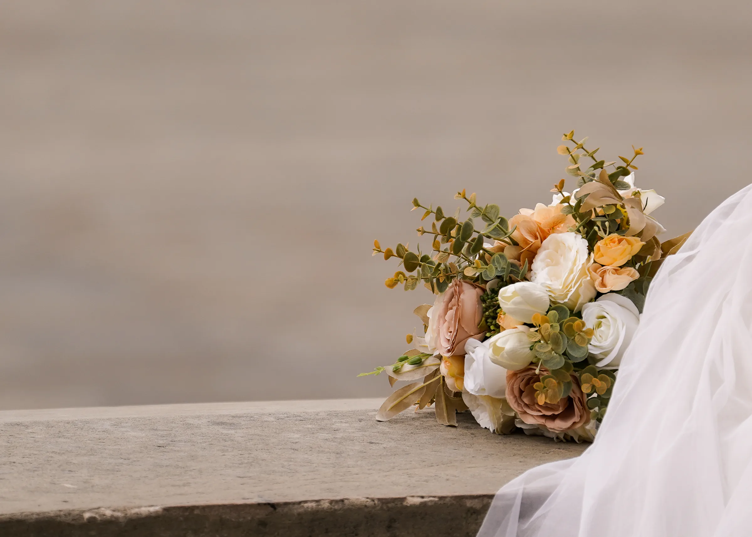 A bridal bouquet of peach and cream roses resting on stone beside a veil