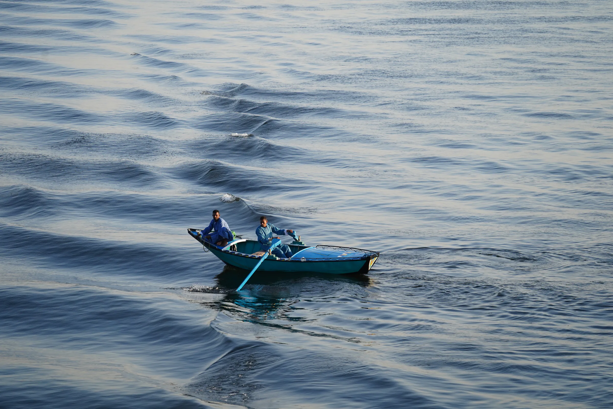 Two men in blue robes crossing calm water in a small blue boat in Egypt