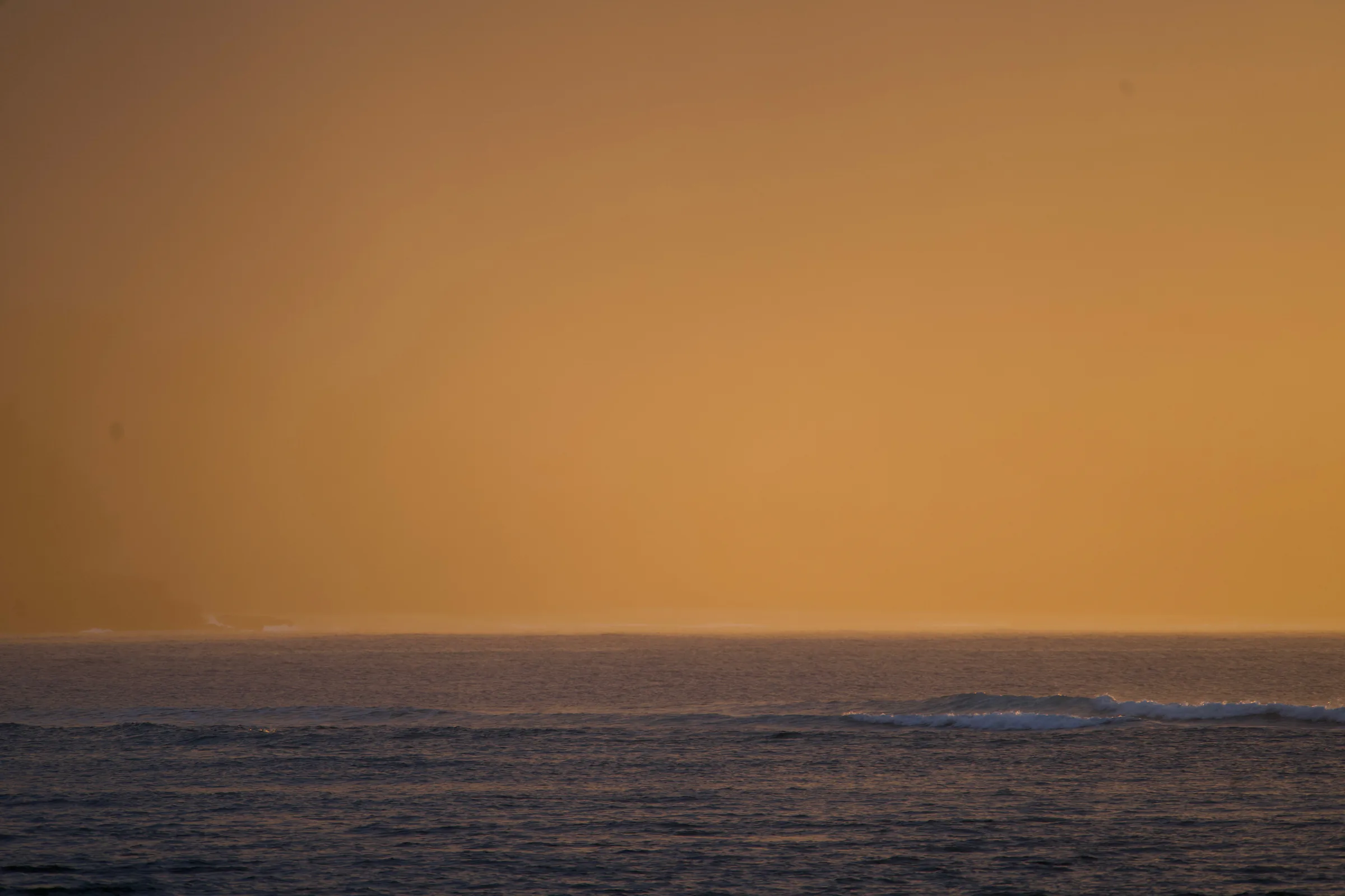 Dark ocean waves beneath a glowing amber sky