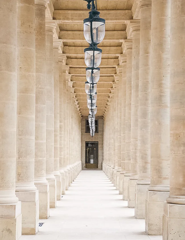 Warm stone colonnade receding to a vanishing point beneath hanging lanterns