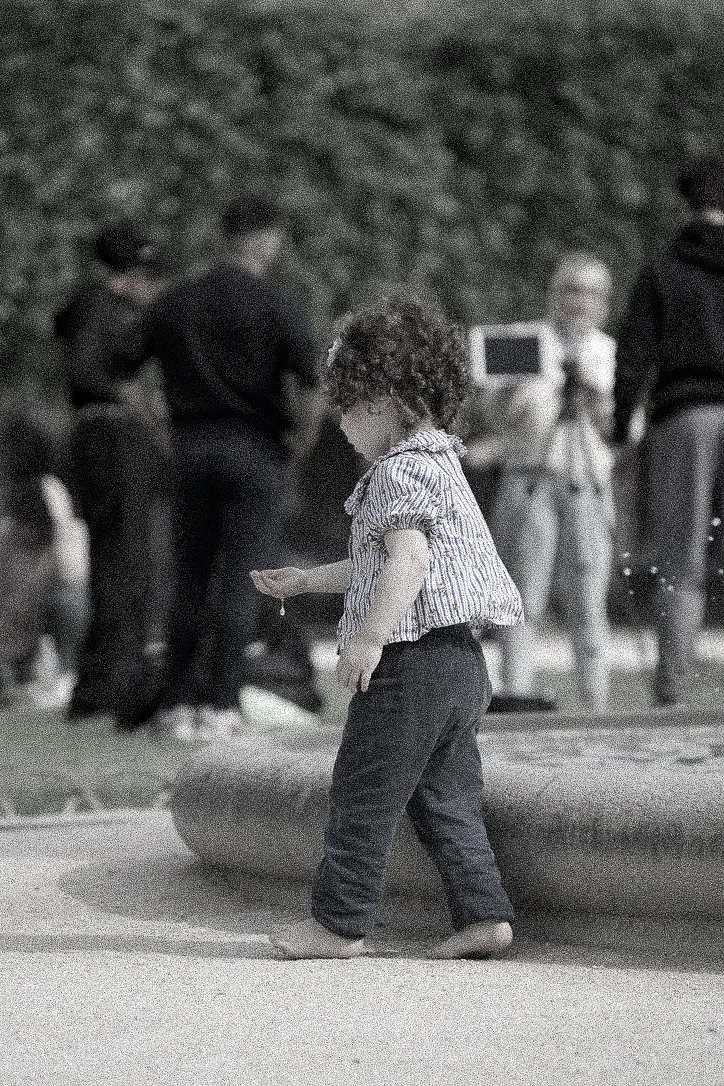 Black and white photograph of a small child walking barefoot beside a stone fountain