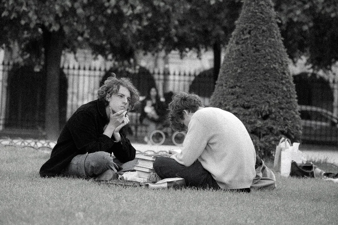 Black and white photograph of two people sitting on the grass with a stack of books between them