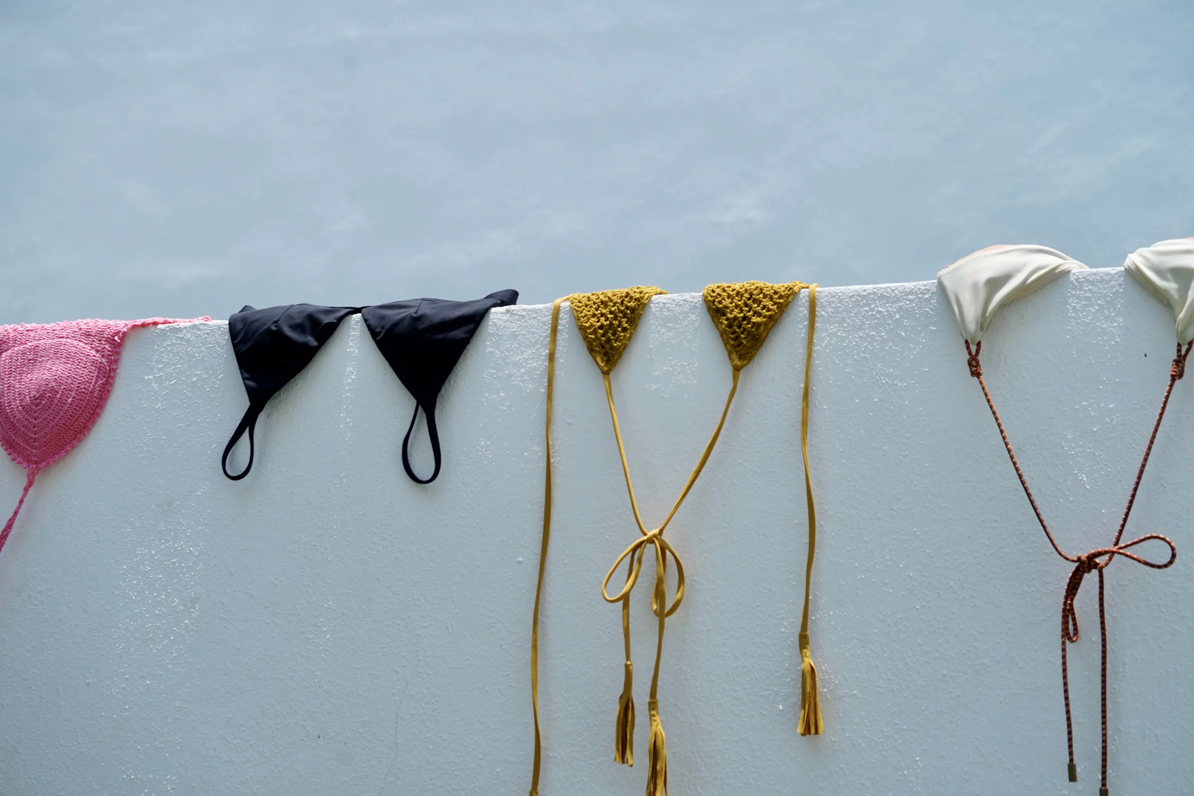 Pink, black, gold, and ivory knit swimwear hanging against a white wall