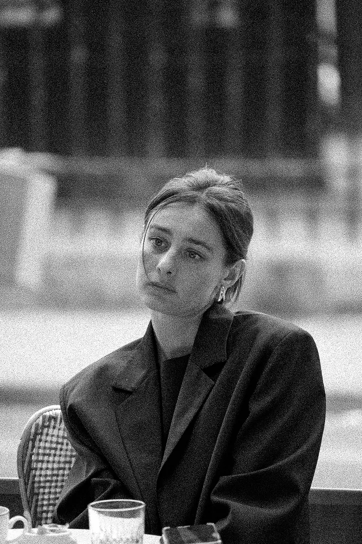 Black and white cafe portrait of a woman in an oversized blazer looking straight into the camera