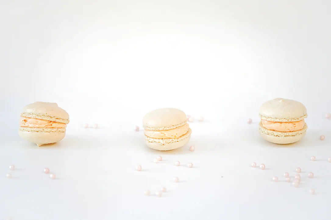 Three pale macarons and sugar pearls arranged on white